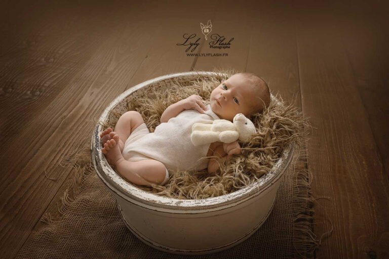 photo de bébé a la naissance dans un beau panier en bois, qui regarde la beauté de la lumière naturelle qui vient réchauffer la scène