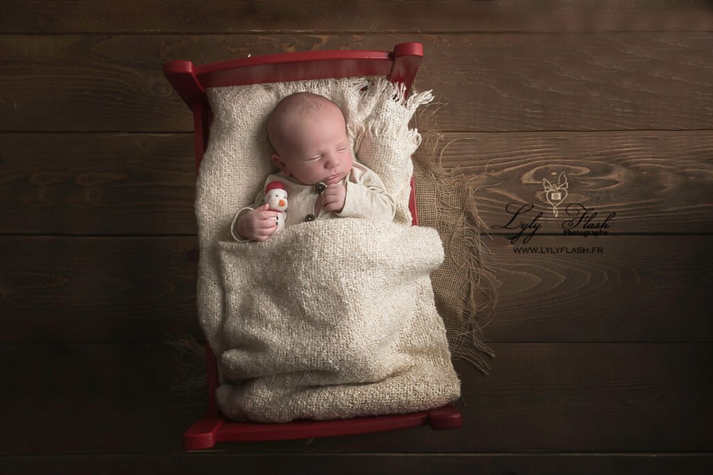 photographie d un bébé né a noël avec son petit lie Rouge et son bonhomme de neige