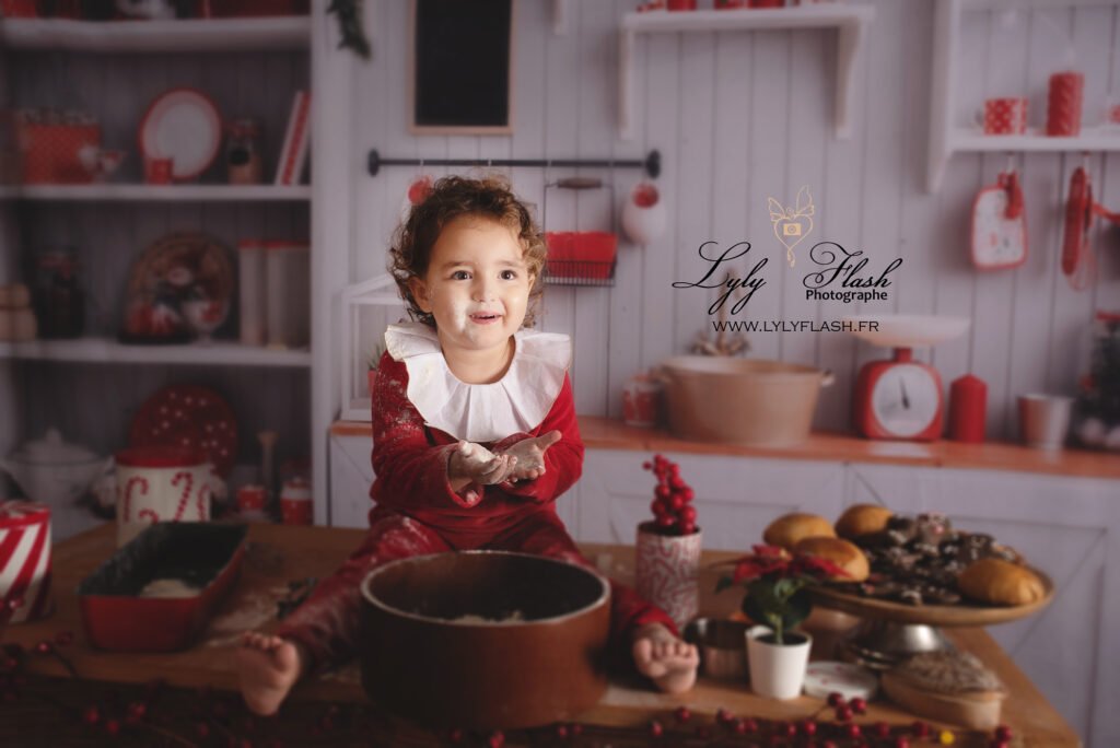 Un bébé de six mois, tout souriant, joue avec des cuillères en bois dans la cuisine de Noël à Saint-Raphaël, sous l'œil bienveillant du Père Noël.