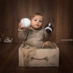 portrait d un bébé en studio sur un fond en bois avec des ballon de foot et de rugby pour la valorisation des sport pendant l enfance