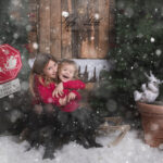 Selfie avec le Père Noël : Deux enfants prennent joyeusement un selfie avec le Père Noël, tous souriants, entourés de cadeaux colorés et de décorations festives dans un salon lumineux.