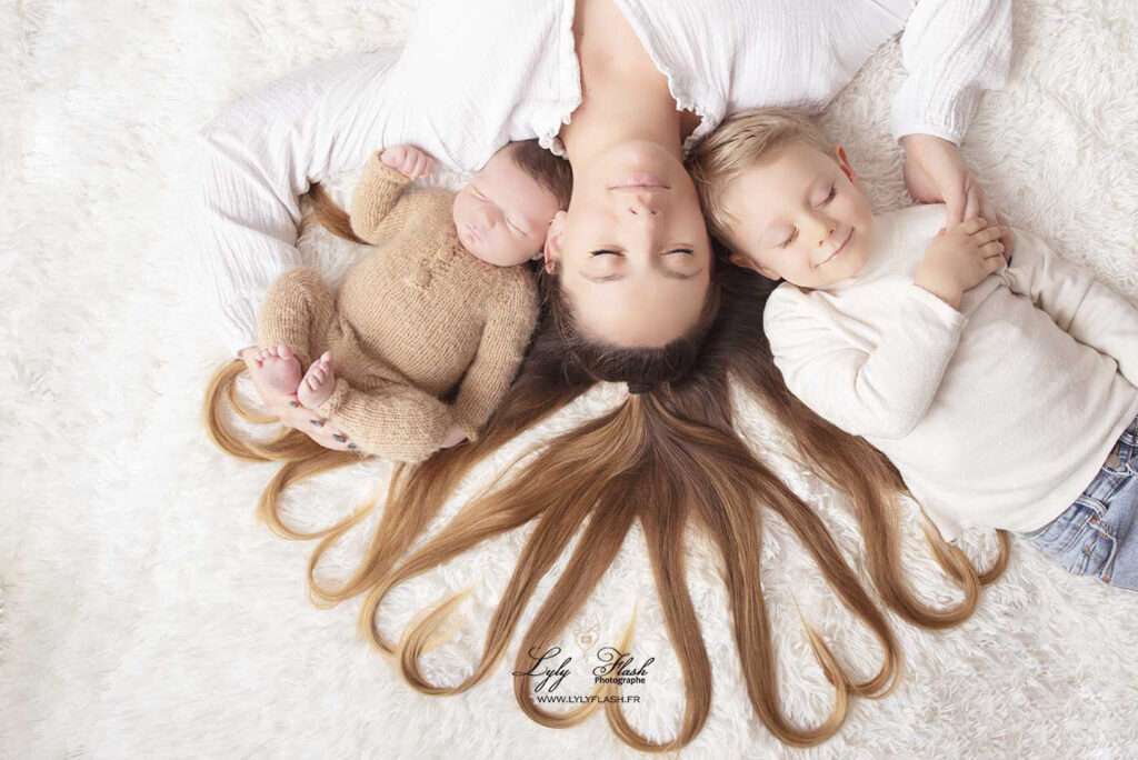 photographie de naissance, un beau petit garçon de 5 jours dans un pyjama en laine de mérinos avec son frère de 2 ans et sa maman. Les cheveux de la maman forment des cœurs pour montrer tout l'amour qu'elle ressent au moment de cette photographe