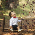 photo d enfant en pleine foret assis sur un petit lit en bois qui s'émerveille des feuille qui volent devant lui en plein automne près de Camps-la-Source