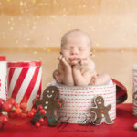 photo de naissance sur le thème de noël. Un nouveau-né en position froggy est posé sur une boite a cookies de noël pour une ambiance chaleureuse