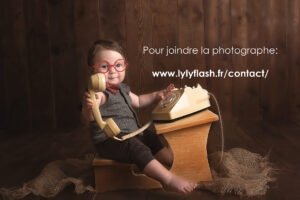 Un beau bébé joue au secrétaire pour le studio photo Lyly flash. C'est trop mignon de le voir porter des lunette rouge et de tendre le combiné du téléphone des année 80, pour vous proposer de contacter la photographe. Une photographie super mignonne pour inciter a contacter la photographe du studio