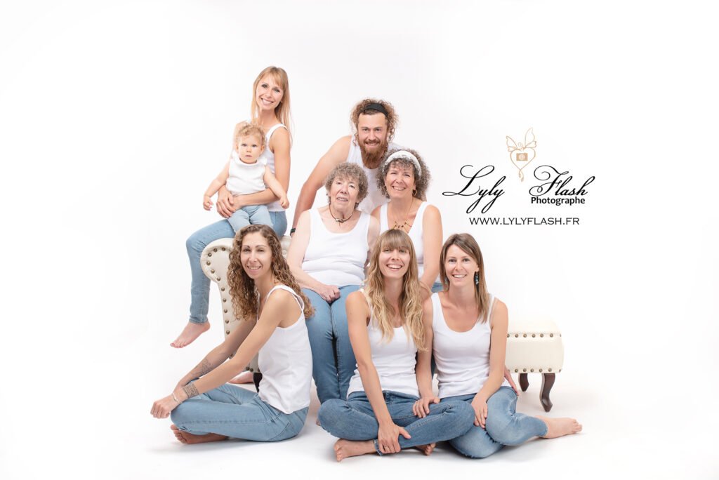 Toute la famille est assise sur le sol, formant un demi-cercle. La grand-mère tient fièrement la petite fille sur ses genoux, entourée de ses filles et son fils, qui sourient vers l'objectif. Les tons doux de la photo créent une atmosphère paisible et chaleureuse.