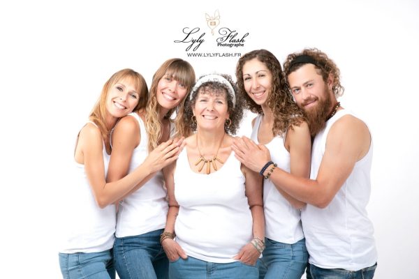 photo-famille-studio-photographe-var ette photo de famille est prise en contre-plongée, donnant un effet majestueux. La grand-mère est assise sur une chaise haute, ses filles et son fils debout à ses côtés, la petite fille tenant la main de la grand-mère, regardant avec émerveillement vers le ciel.